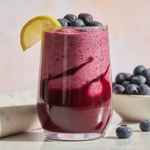 Tall glass of vibrant purple lemon-blueberry smoothie, garnished with fresh blueberries and a lemon wedge