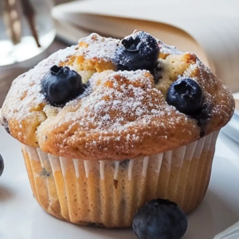 A golden blueberry protein muffin with fresh blueberries on a plate.