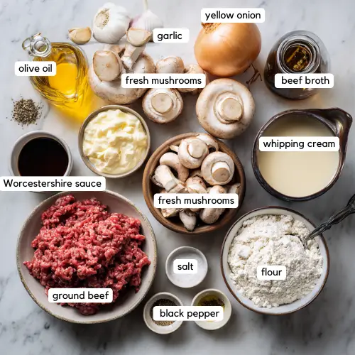 Top-down view of labeled ingredients for ground beef stroganoff including ground beef, fresh mushrooms, garlic, yellow onion, olive oil, Worcestershire sauce, beef broth, whipping cream, flour, salt, and black pepper