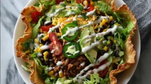 Overhead view of a taco salad bowl in a tortilla shell with fresh toppings.
