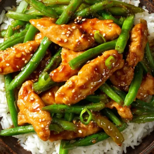 Top-down view of string bean chicken Panda Express copycat served with steamed white rice in a black bowl on a bamboo mat