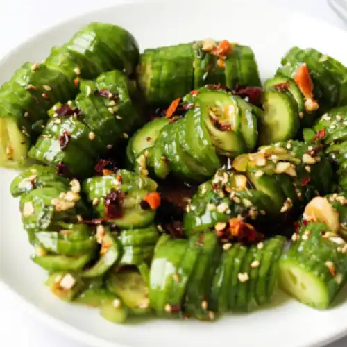 Close-up of Asian cucumber salad on a white plate, made with spiral-cut cucumbers tossed in soy sauce, chili oil, garlic slices, and sesame seeds.