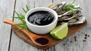 Oyster sauce in a white bowl with fresh oysters and lime on rustic wood