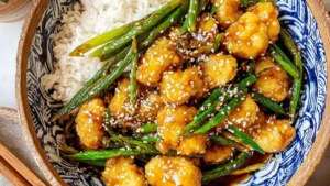 Crispy honey sesame chicken with sesame seeds and veggies served on rice in a bowl