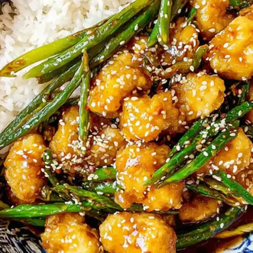 Crispy honey sesame chicken with sesame seeds and veggies served on rice in a bowl