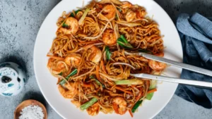 Bowl of shrimp lo mein with noodles, shrimp, and vegetables styled with chopsticks.