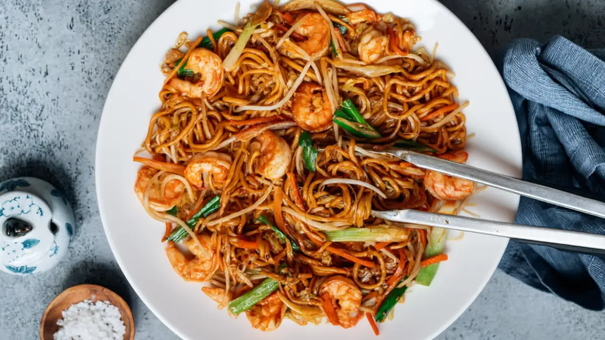 Bowl of shrimp lo mein with noodles, shrimp, and vegetables styled with chopsticks.