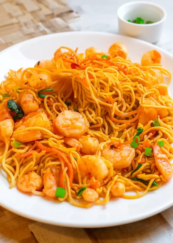 Plate of shrimp lo mein with noodles, shrimp, and scallions on a white dish.