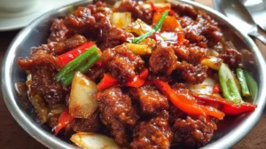 Crispy Beijing Beef in sweet tangy sauce with red bell peppers, onions, and green onions served in a bowl.