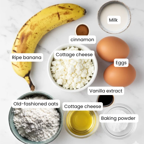 Cottage cheese, banana, oats, eggs, milk, and cinnamon arranged in bowls on a kitchen counter.