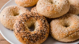 Freshly baked protein bagels topped with sesame seeds and everything seasoning on a white plate.