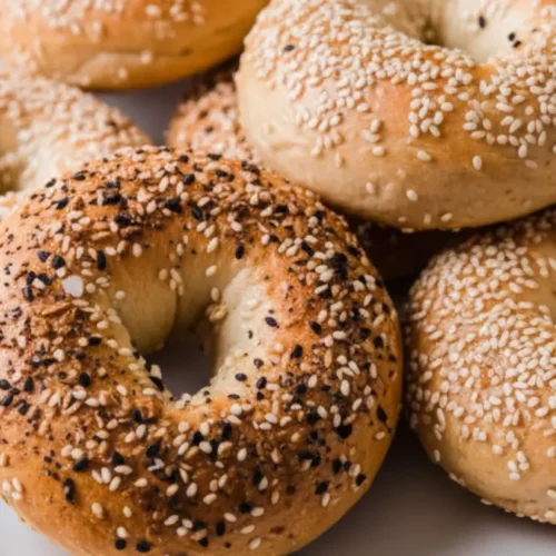 Freshly baked protein bagels topped with sesame seeds and everything seasoning on a white plate.