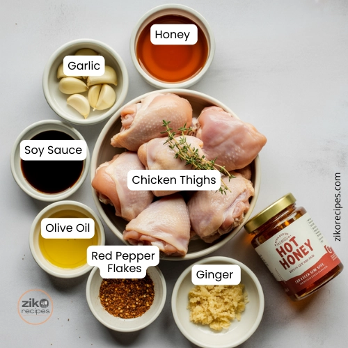 Flat lay of chicken thighs, garlic, honey jar, soy sauce, and fresh herbs