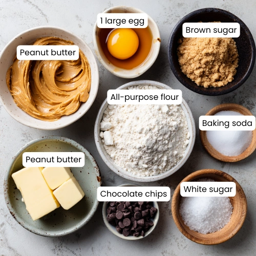 Flat lay of peanut cookie ingredients including peanut butter, flour, sugars, butter, egg, and chocolate chips.