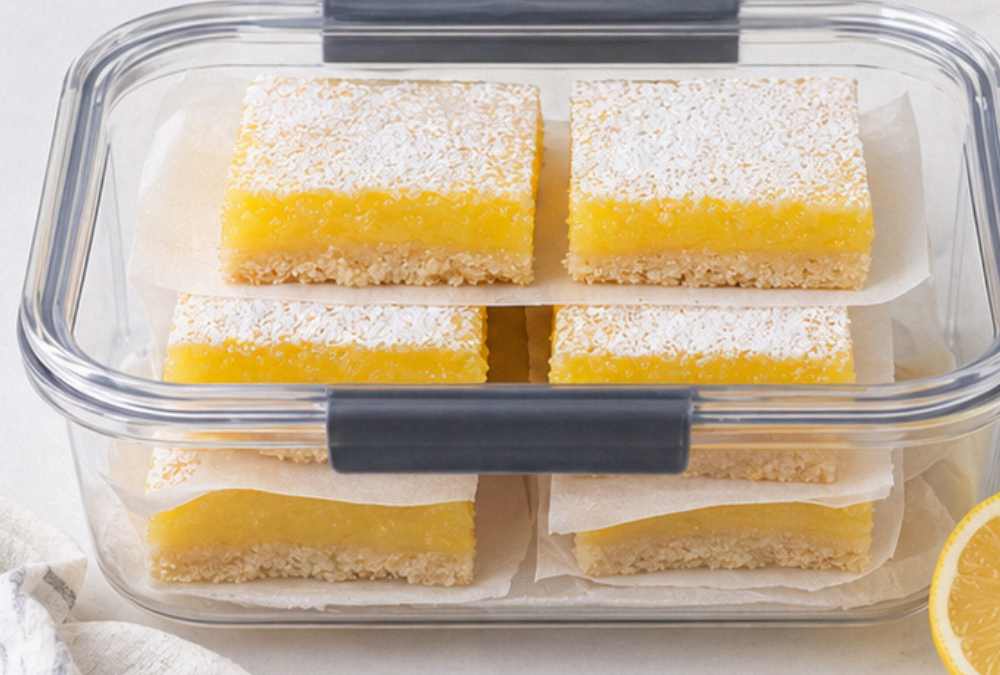 Easy lemon bars stored in a glass airtight container with parchment paper between layers