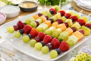 Colorful fruit skewers for parties on a platter with strawberries, grapes, pineapple, melon, and blueberries