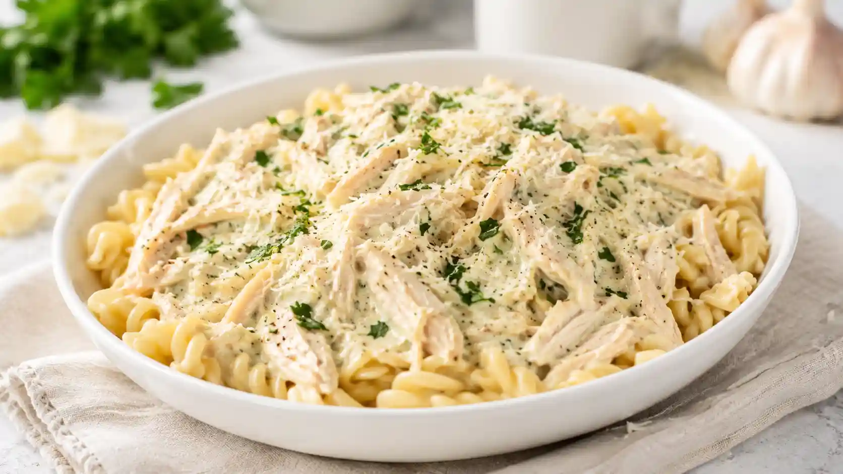 Creamy garlic parmesan chicken served over pasta with parmesan, parsley, and a rich sauce in a white bowl.