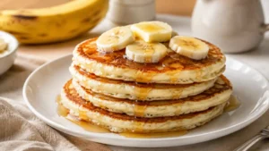 Fluffy banana pancakes stacked with sliced bananas and maple syrup for an easy breakfast.