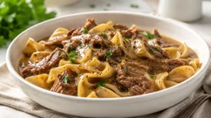 A cozy bowl of crockpot beef and noodles with tender beef, wide egg noodles, savory gravy, black pepper, and parsley.