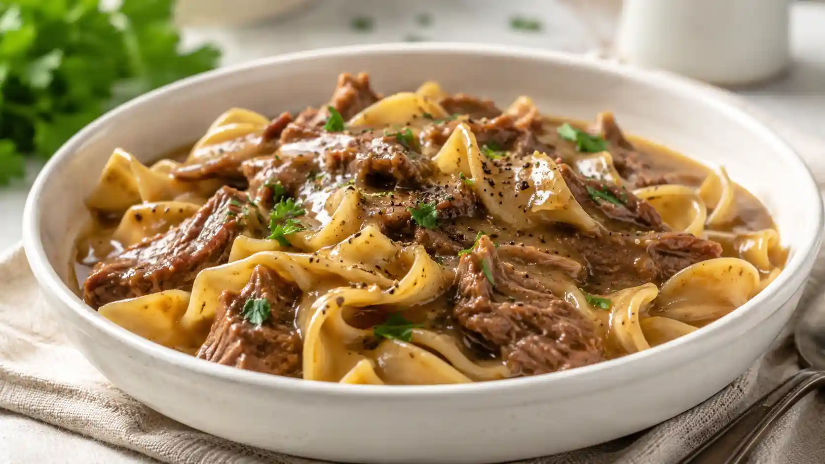 A cozy bowl of crockpot beef and noodles with tender beef, wide egg noodles, savory gravy, black pepper, and parsley.