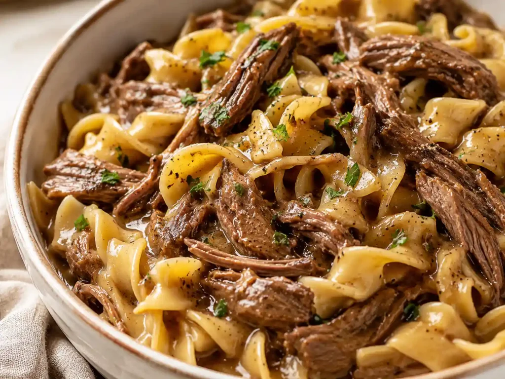 Close-up of tender beef, wide egg noodles, and thick savory gravy showing the texture of crockpot beef and noodles.