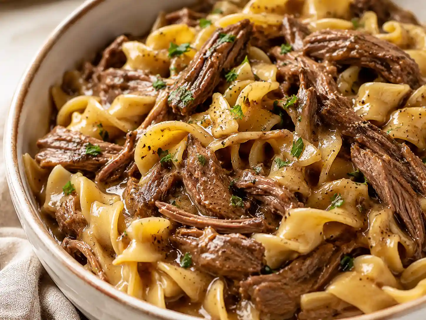 Close-up of tender beef, wide egg noodles, and thick savory gravy showing the texture of crockpot beef and noodles.