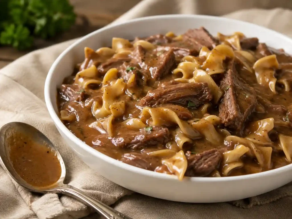 A bowl of crockpot beef and noodles with thick gravy coating the noodles and beef.
