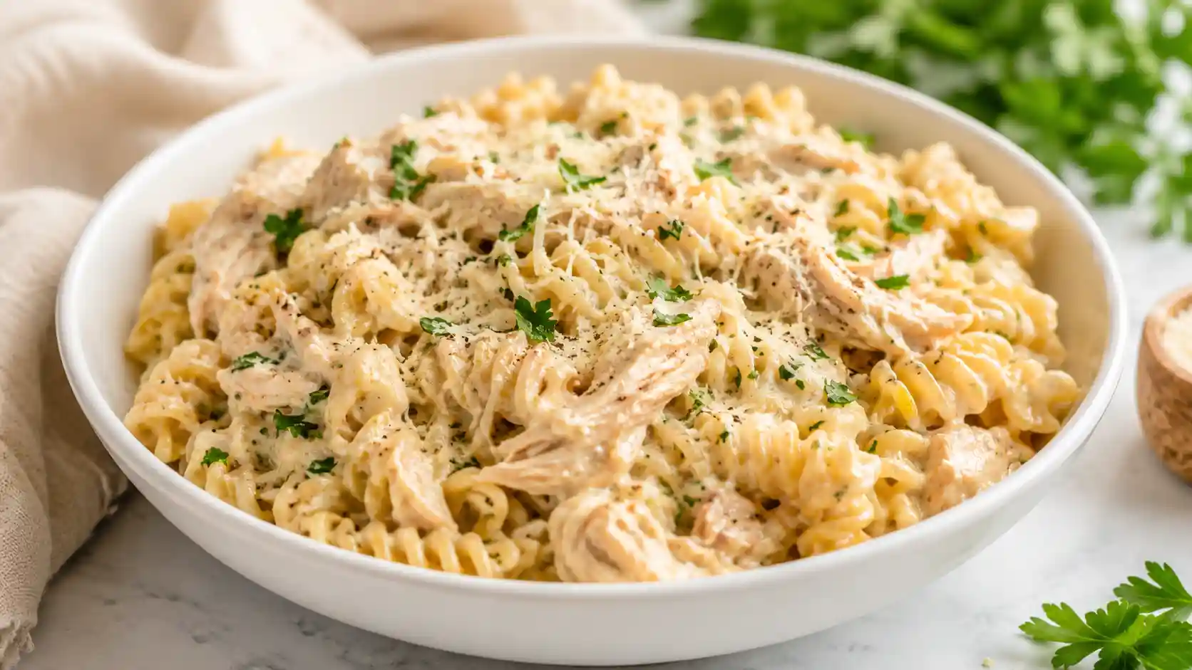 Creamy crockpot garlic parmesan chicken pasta with shredded chicken, rotini, Parmesan, and parsley in a white bowl.