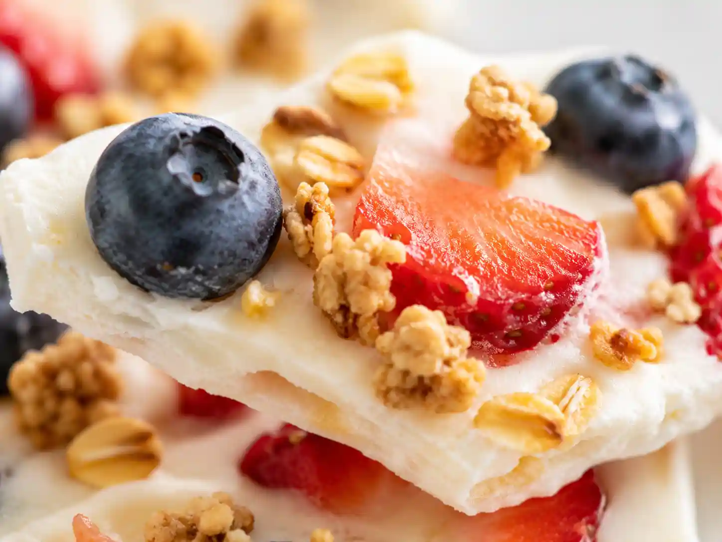 Close-up of frozen yogurt bark showing creamy yogurt, strawberries, blueberries, and crunchy granola