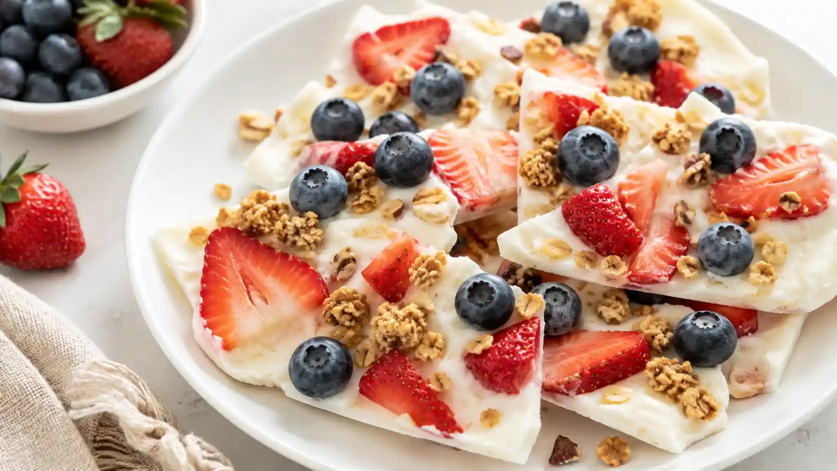 Frozen yogurt bark with strawberries, blueberries, and granola on a white plate