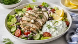 Greek chicken salad with tzatziki, sliced chicken, romaine, cucumber, tomatoes, olives, feta, lemon, and dill