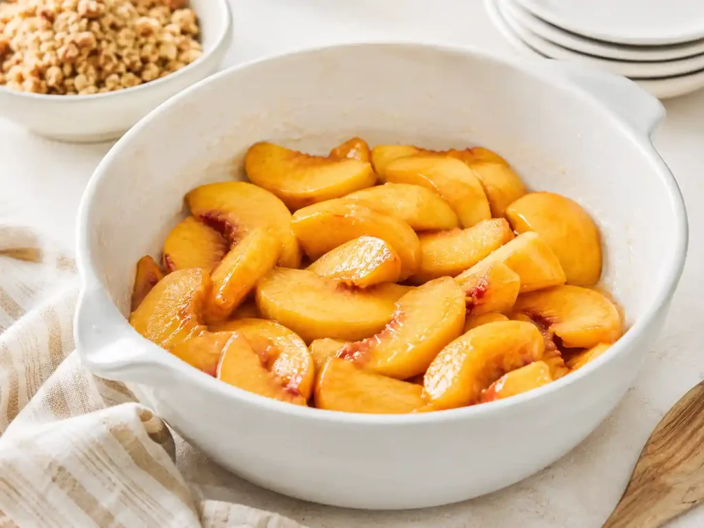 Sliced peaches mixed with sugar, lemon juice, vanilla, and cornstarch in a mixing bowl.