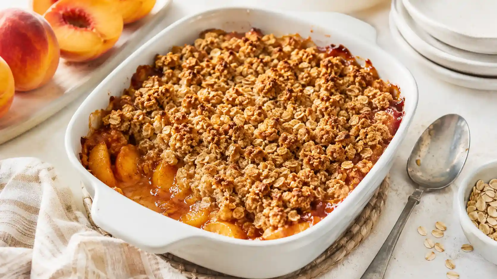 Warm peach crisp with golden oat topping served in a white baking dish.