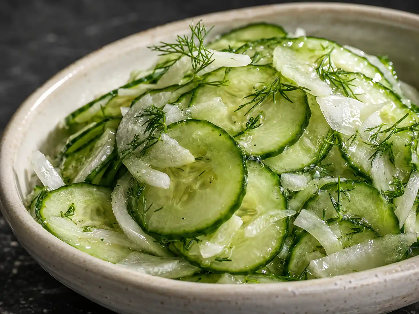 Sharp close-up of crisp cucumber slices and onions coated in a clear vinegar dressing.