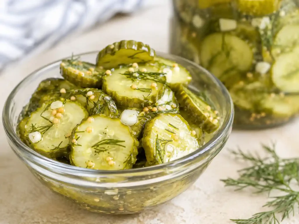 Sharp close-up of crisp refrigerator pickle chips with dill and garlic in a clear brine.
