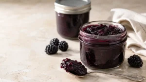 Homemade blackberry jam in a clear glass jar with fresh ripe blackberries and a spoonful of thick jam.